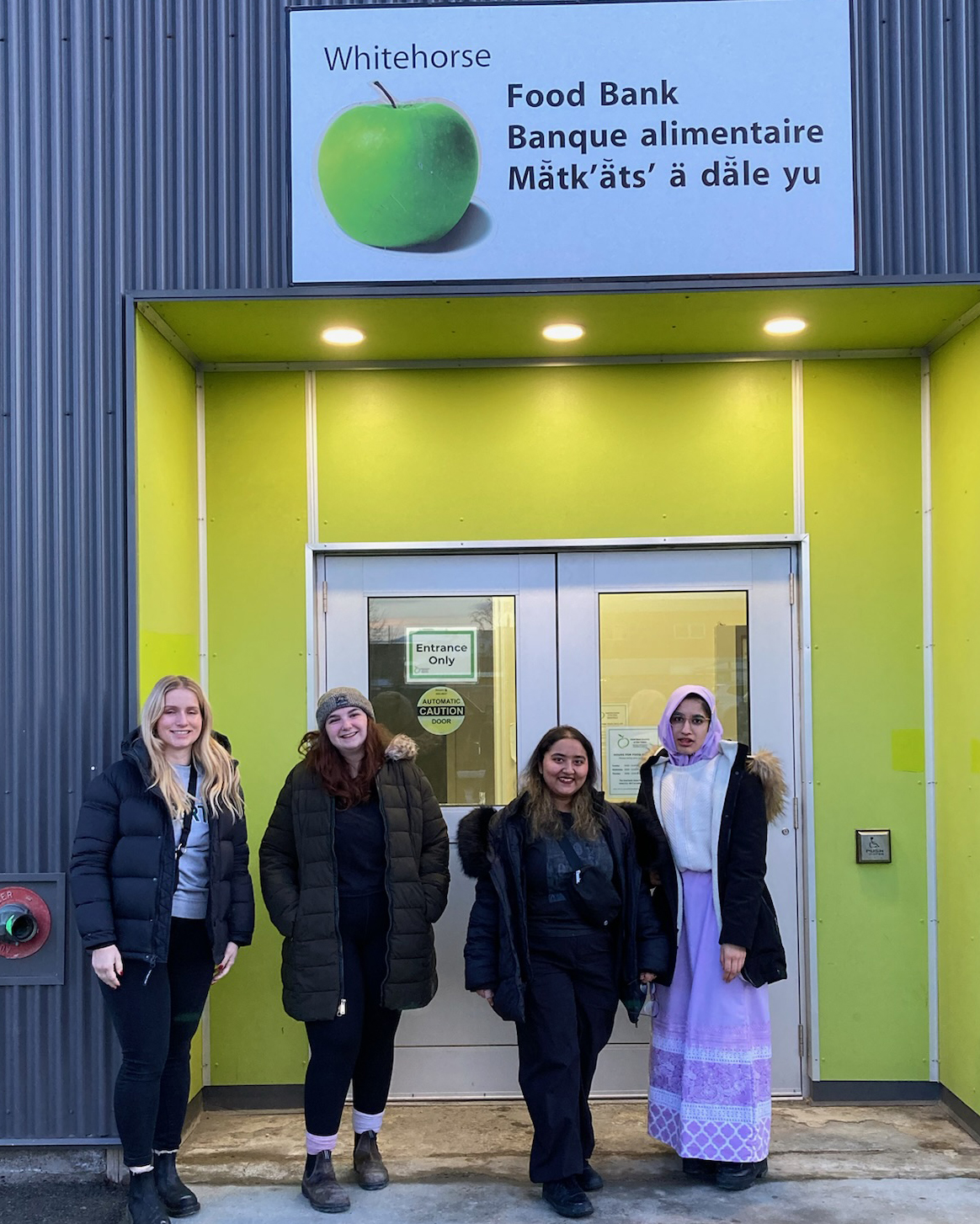Four students pose outside the Yukon Food Bank building