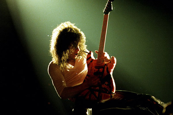 A photo of Eddie Van Halen playing guitar on stage under a green light.