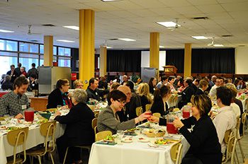 A photo of a full dining hall with tablecloths and people sitting at the tables.