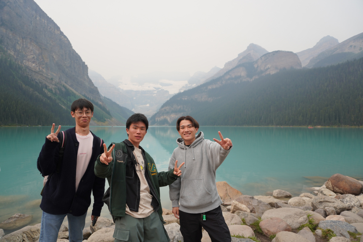 Group of 3 students outdoors in front of mountains and a lake