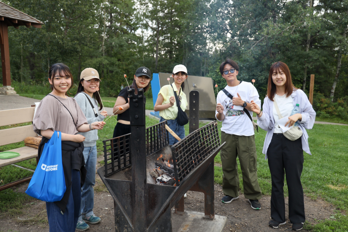 Group of ELS students grilling hot dogs over a fire outdoors