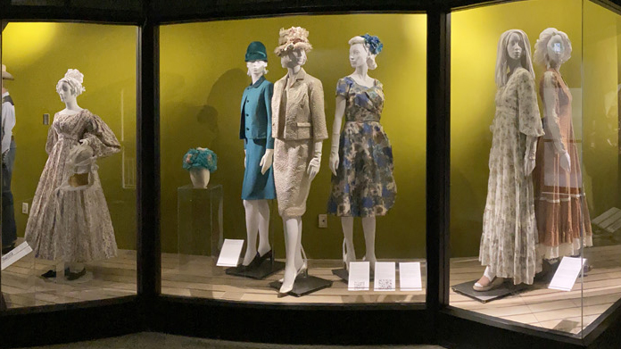 Photo of exhibition showing antique clothes on mannequins behind glass