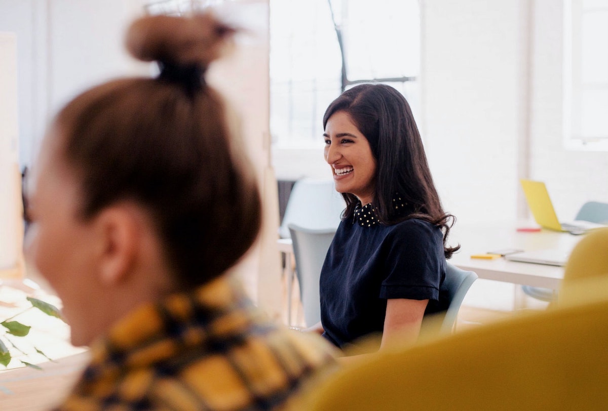 Two women in an office setting are pictured. One woman is in focus and smiling.