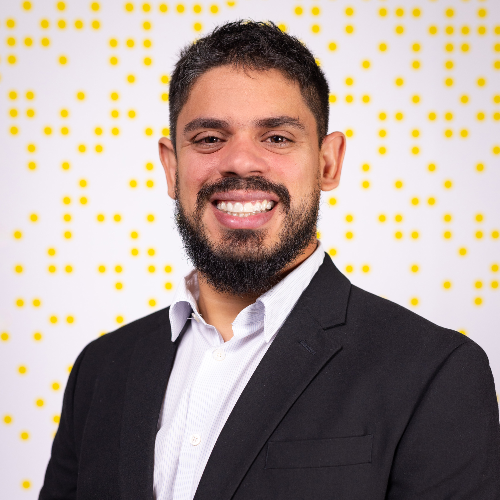 Erick poses wearing a professional blazer in front of a branded U of A backdrop