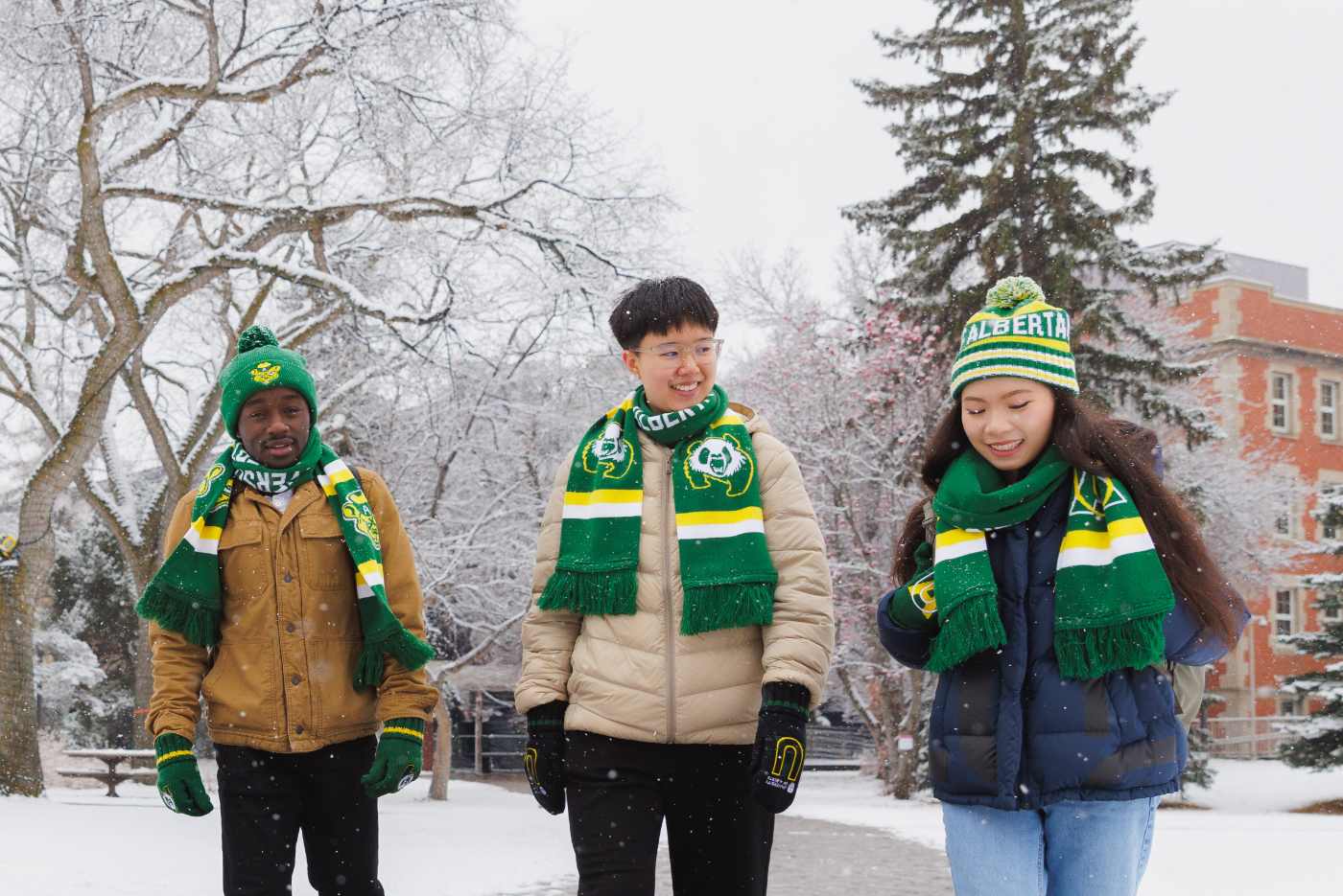 Three students walking on campus in winter green and gold gear