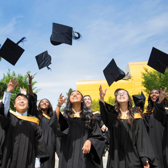 New grads throw their caps into the air on a sunny day.