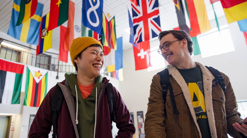 Two international students walking in front of many flags hanging from the ceiling