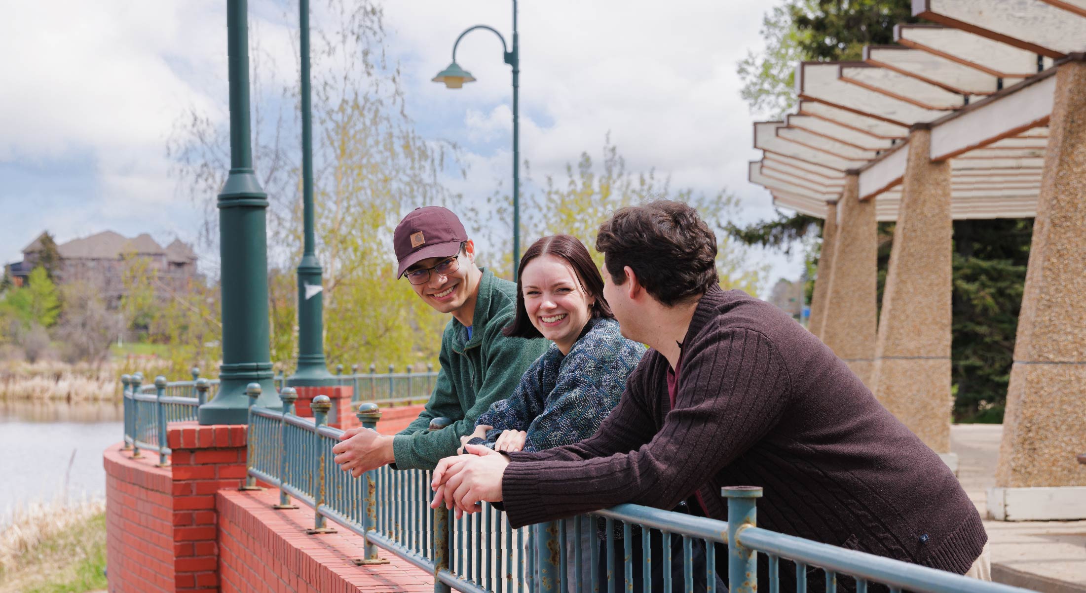 Three students leaning on a rail chatting and looking at the scenery