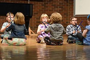 Six children sitting on the floor with sticks.