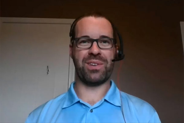 Augustana chemistry professor Brian Rempel sits in front of his computer at home wearing a blue shirt, glasses, and a headset.