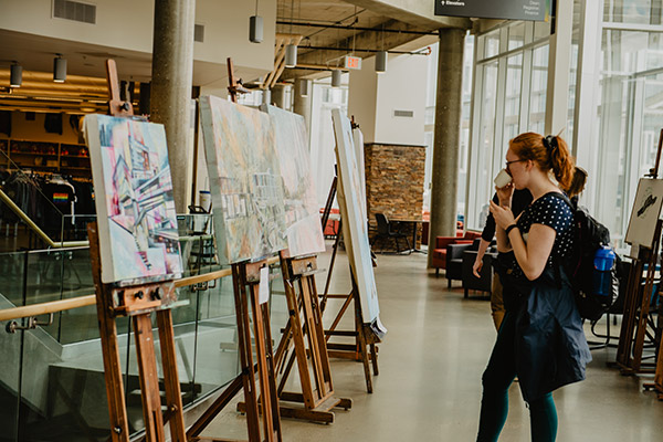 A student holds a cup of coffee while viewing art in the Augustana forum.