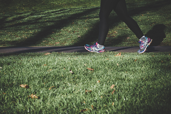 A person wearing bright running shoes is walking through a path surrounded by green grass on each side.