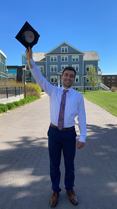 A photo of Thomas Zimmerman holding a grad cap in front of Founders' Hall.