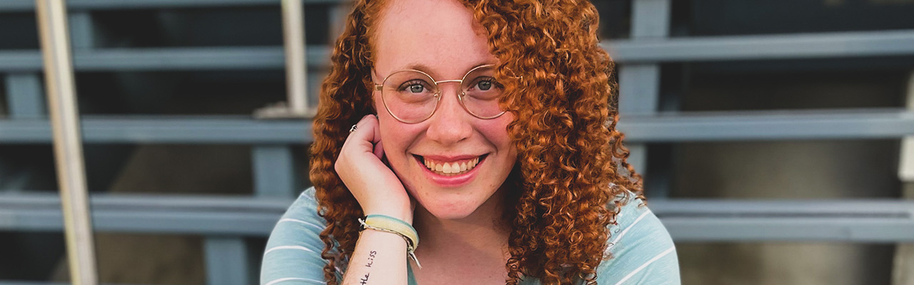 Rebekah Stretch sitting on the steps of Founders' Hall, smiling at the camera as she leans her cheek on her closed hand.