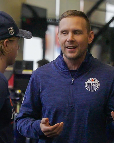 Joel Jackson speaking to someone while wearing an Oilers half-zip sweater.