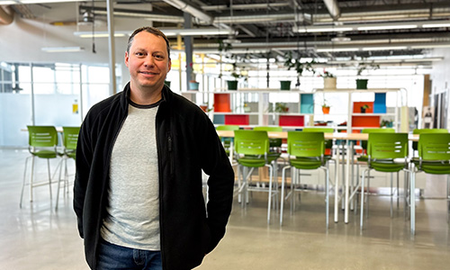 A man standing in a brightly lit, open study space, smiling at the camera.