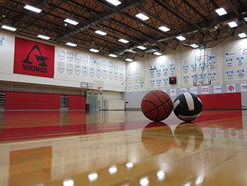 A photo of a basketball and volleyball sitting on the gym floor, taken from floor level.