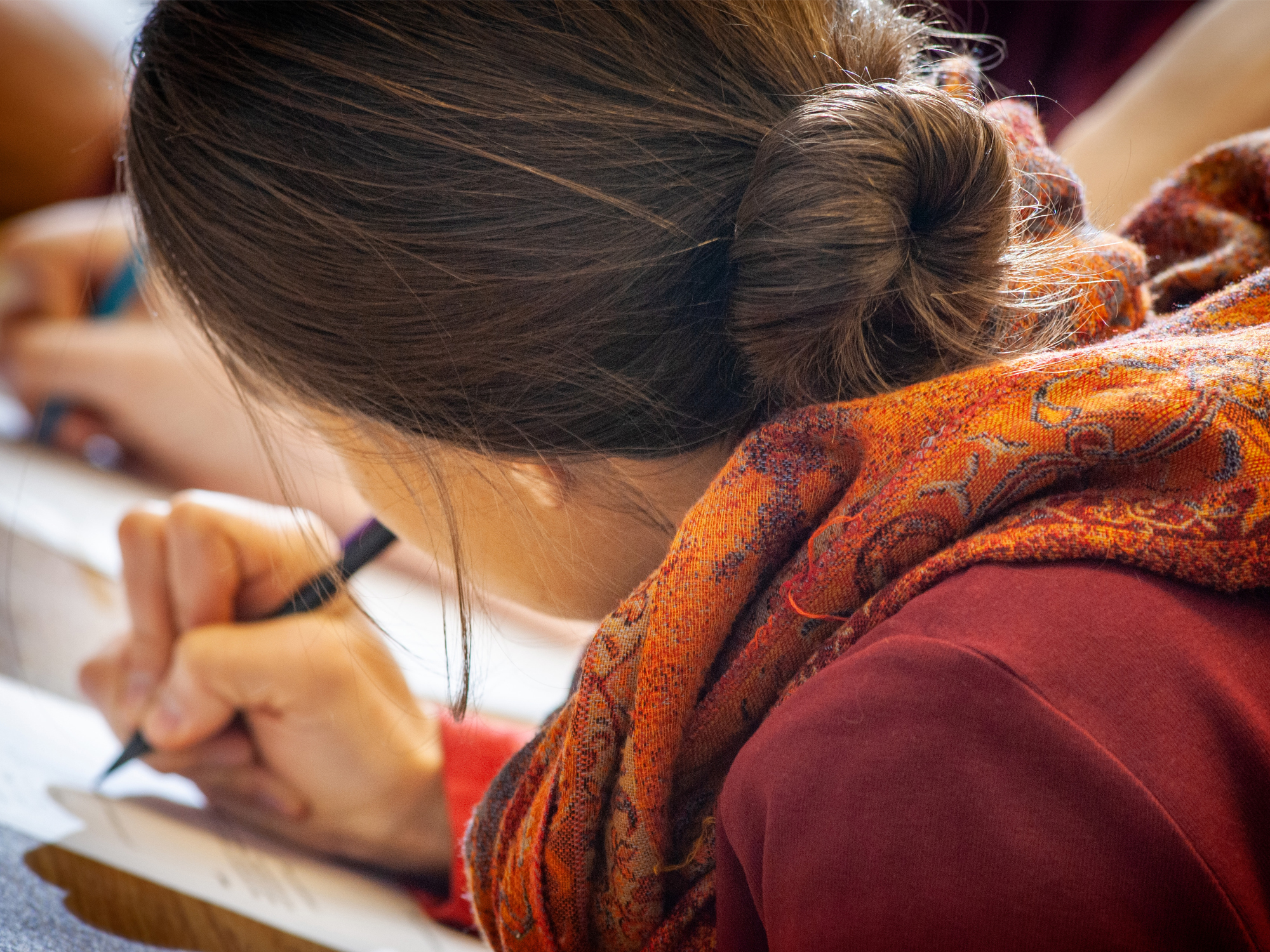 A close- up view over the shoulder of a woman writing with a pen