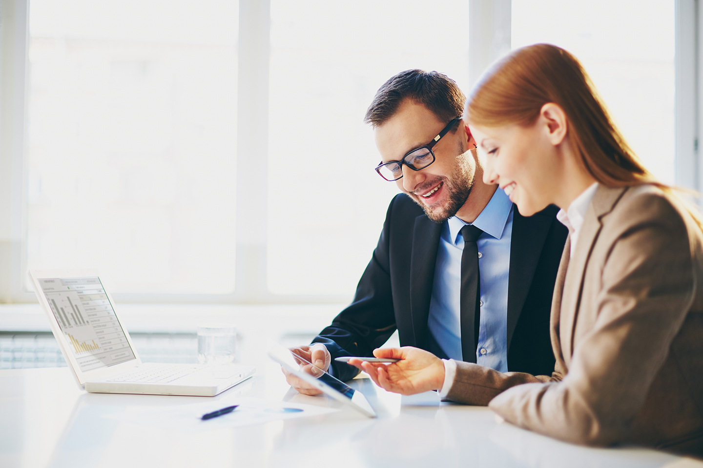 Pic of a man or a woman sitting at a table and comparing graphs on a computer.