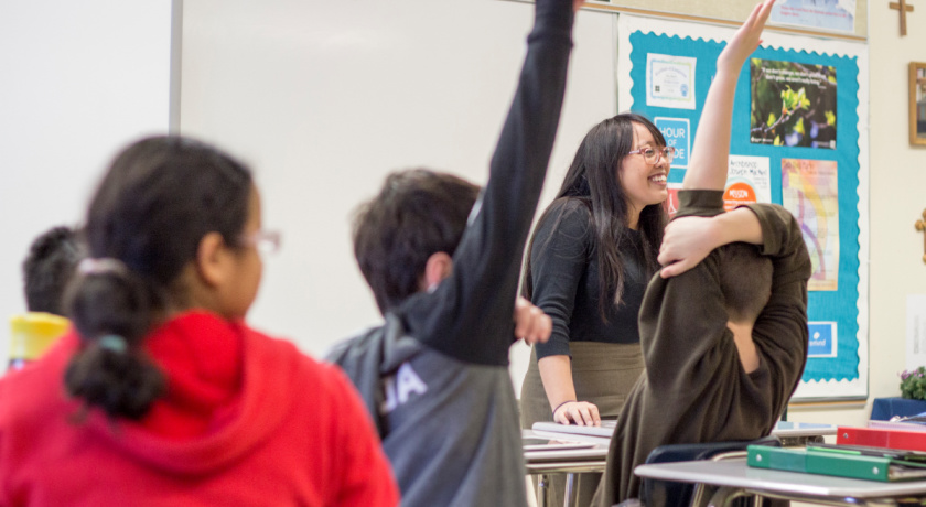 student teacher in front of students with their hands raised