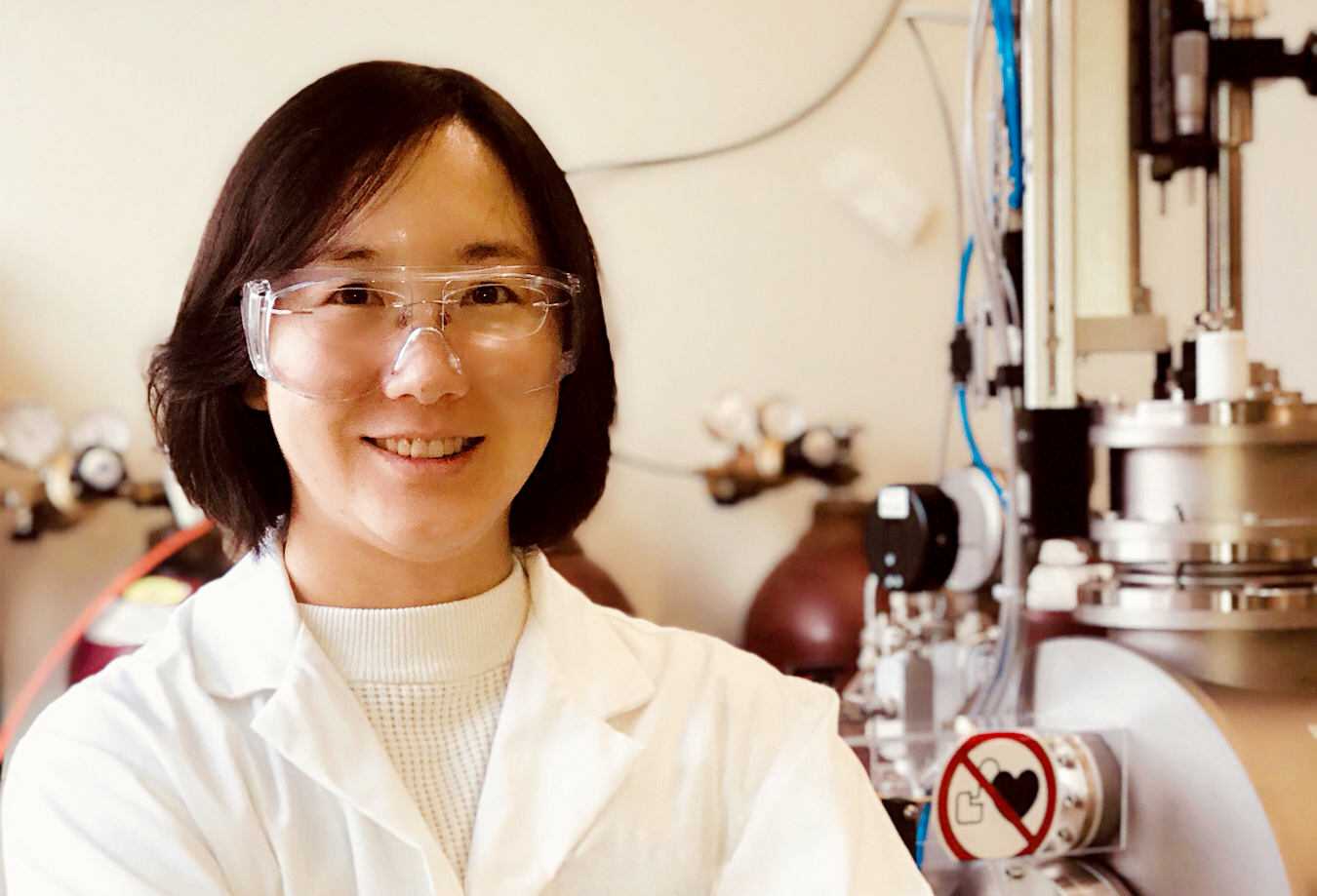 Bing in lab coat and goggles in front of lab equipment.