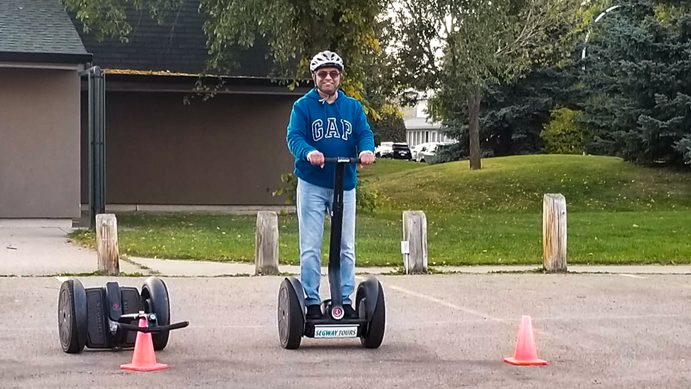 A man rides a segway, smiling, at a community league event