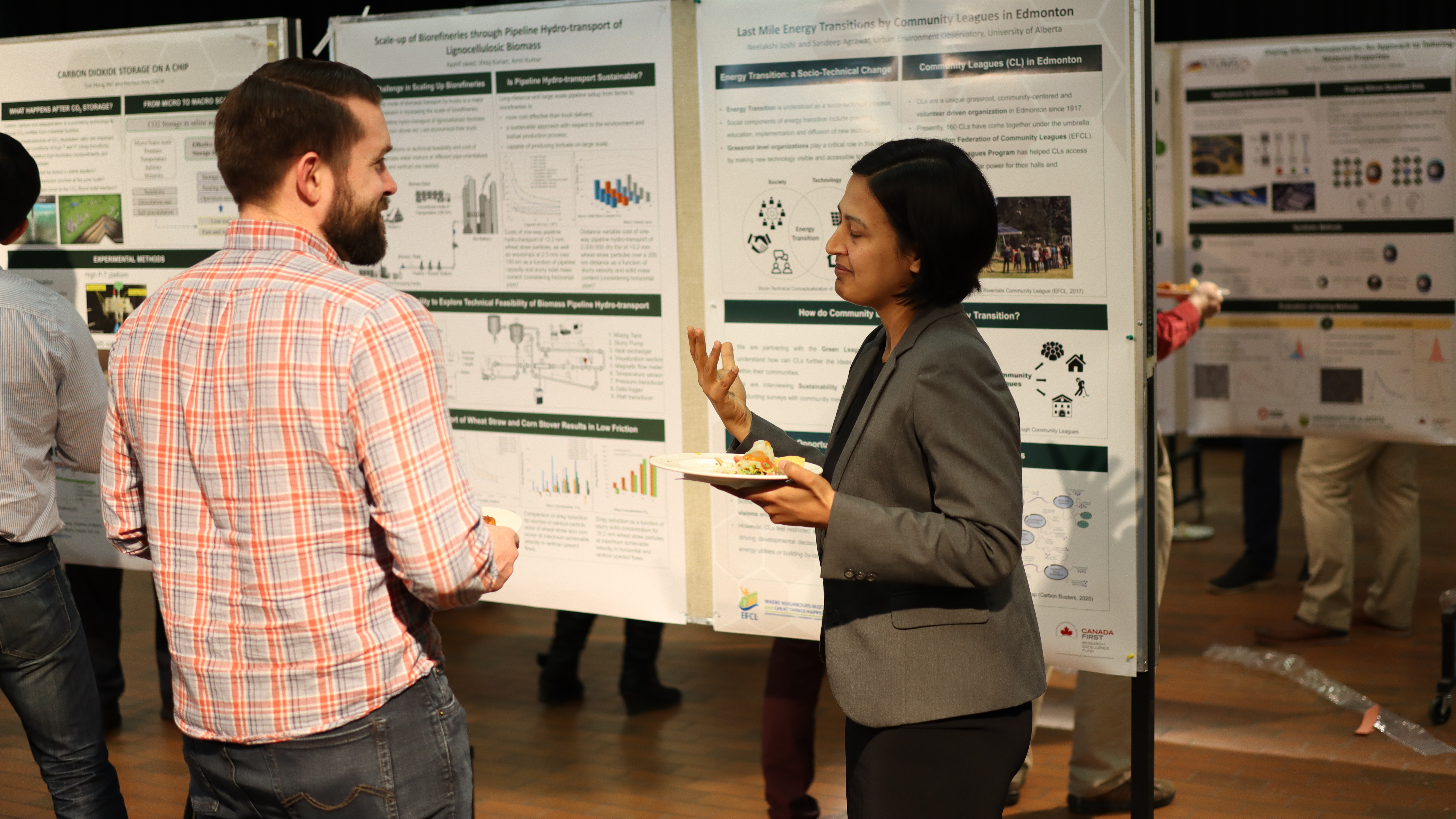 In front of her research poster, Dr. Neelakshi Joshi discusses her work with a young man