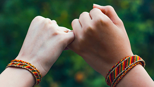 Two hands holding pinkies while wearing bracelets