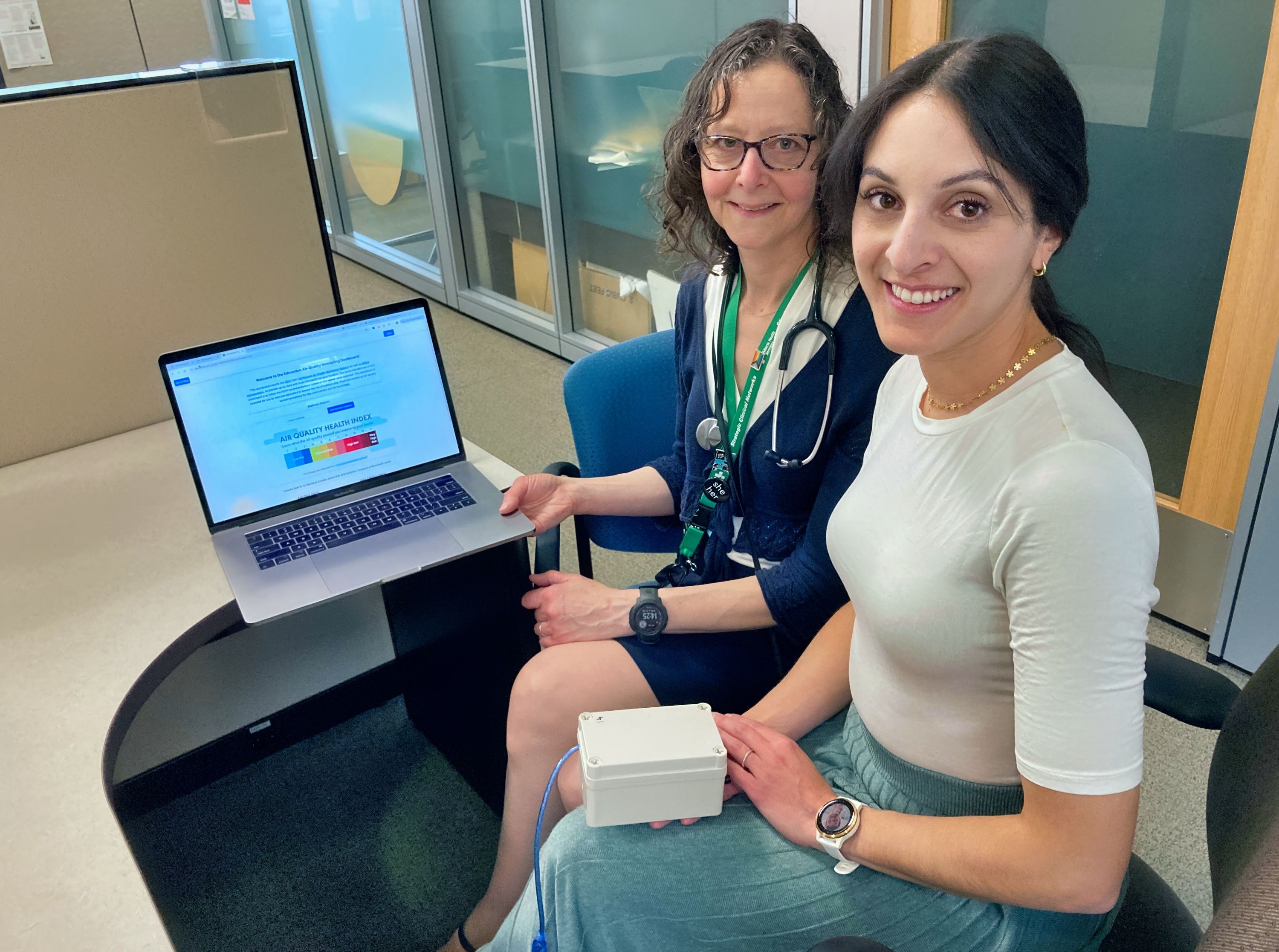 U of A researchers Amina Hussein (front) and Anne Hicks are pictured at a desk with the Government of Canada's Air Quality Health Index showing on a computer monitor. (Photo: Bev Betkowski)