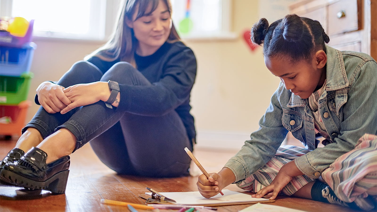 A child drawing while supervised by her teacher