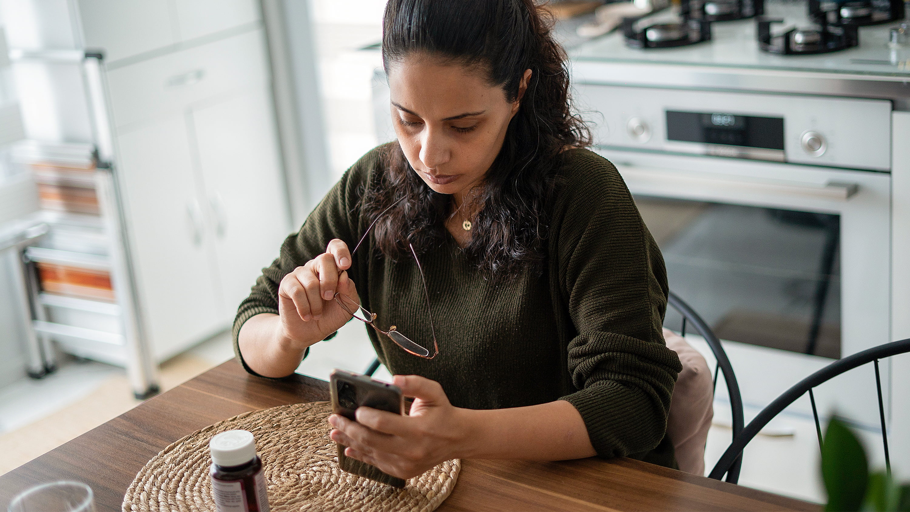 Woman sits in kitchen looking at phone. (Photo: Getty Images)  