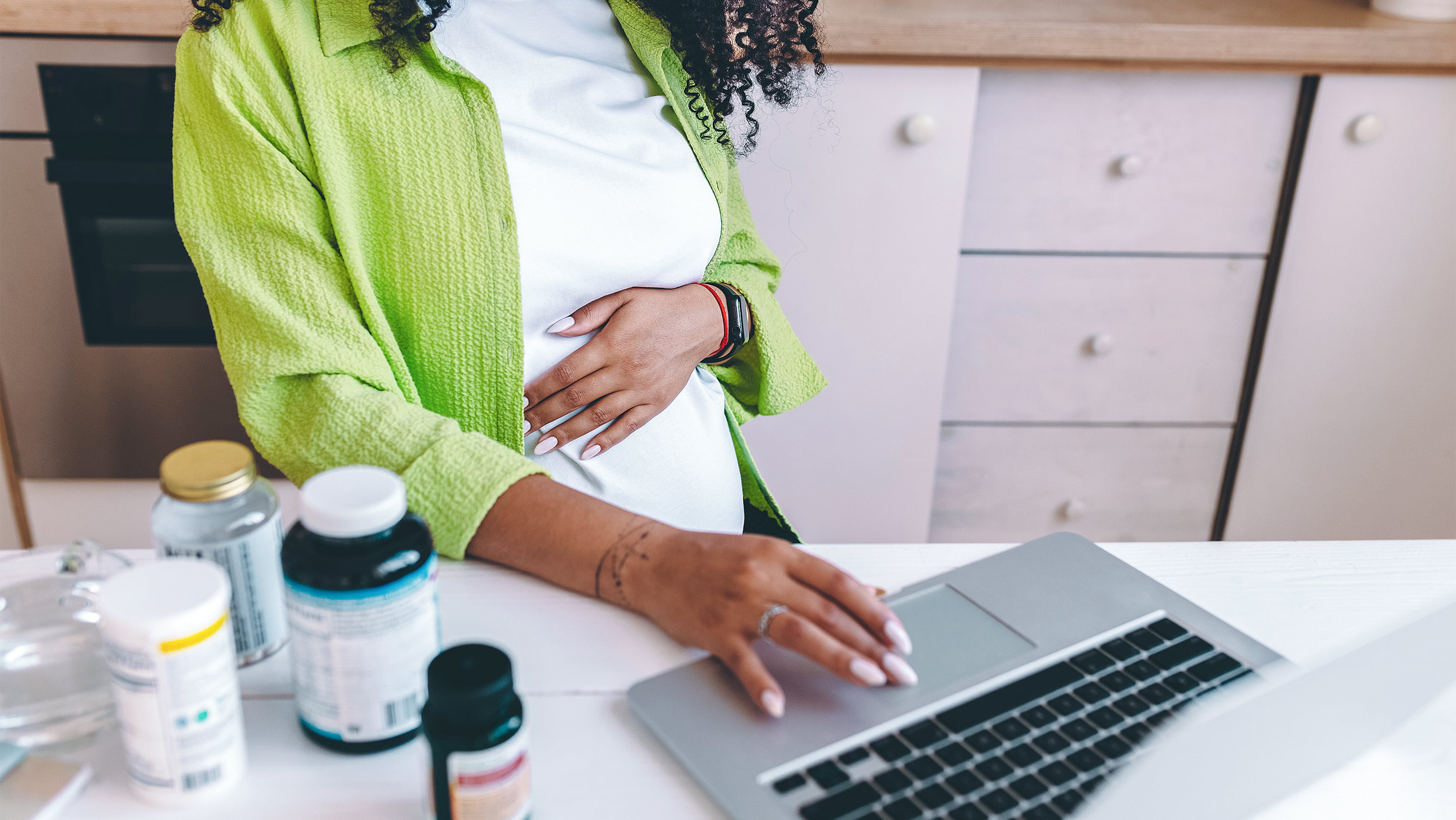 Pregnant woman rubs belly while looking at laptop screen. (Photo: Getty Images)