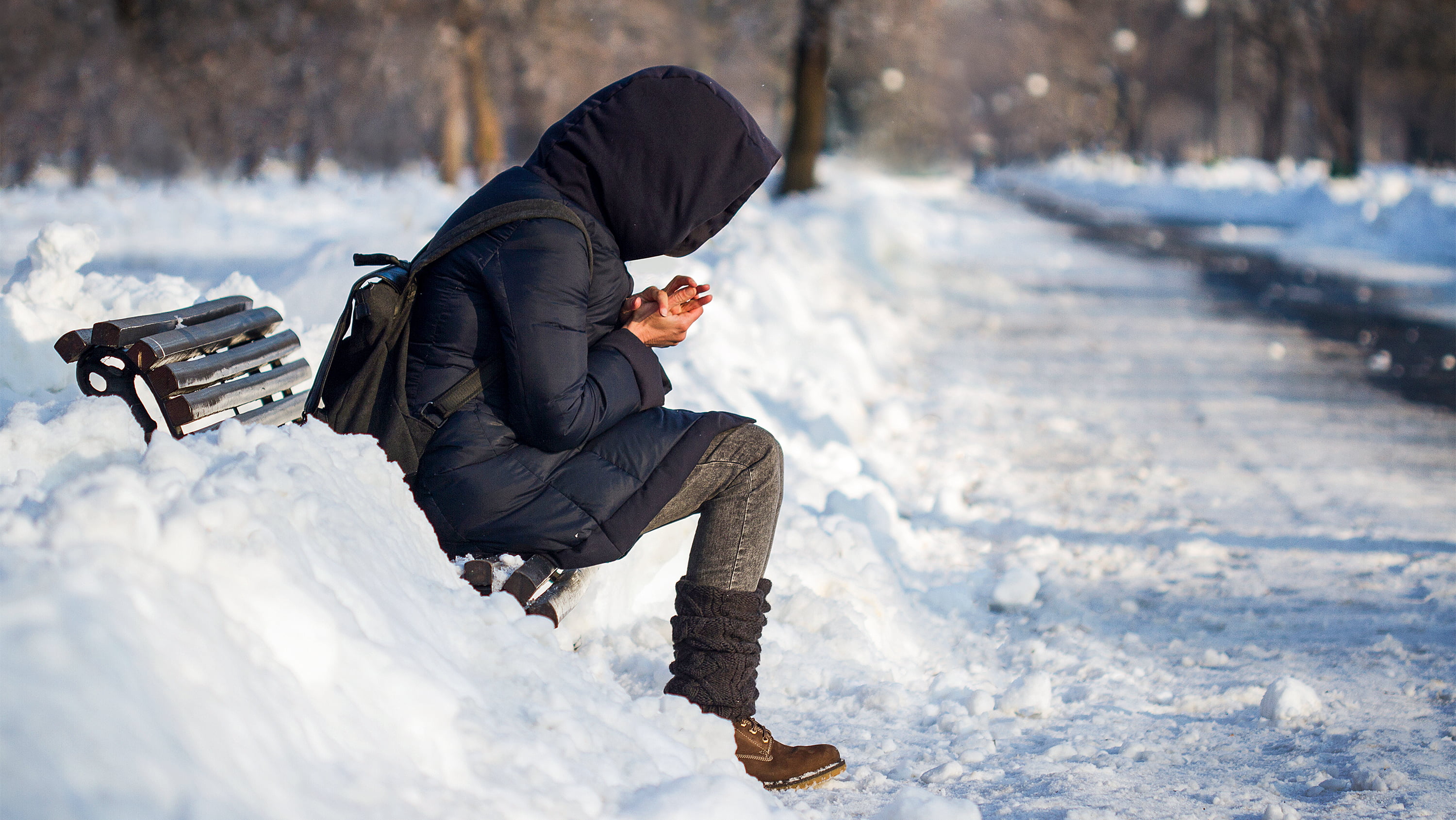 Person in black winter coat sits on park bench in snowy setting. (Photo: Getty Images)