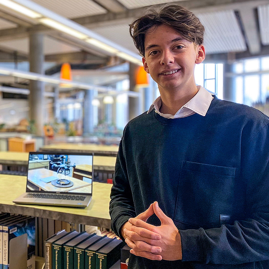 Young man stand in a library showing off a computer with research on the screen