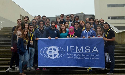 People standing on stairs holding banner that says IFMSA