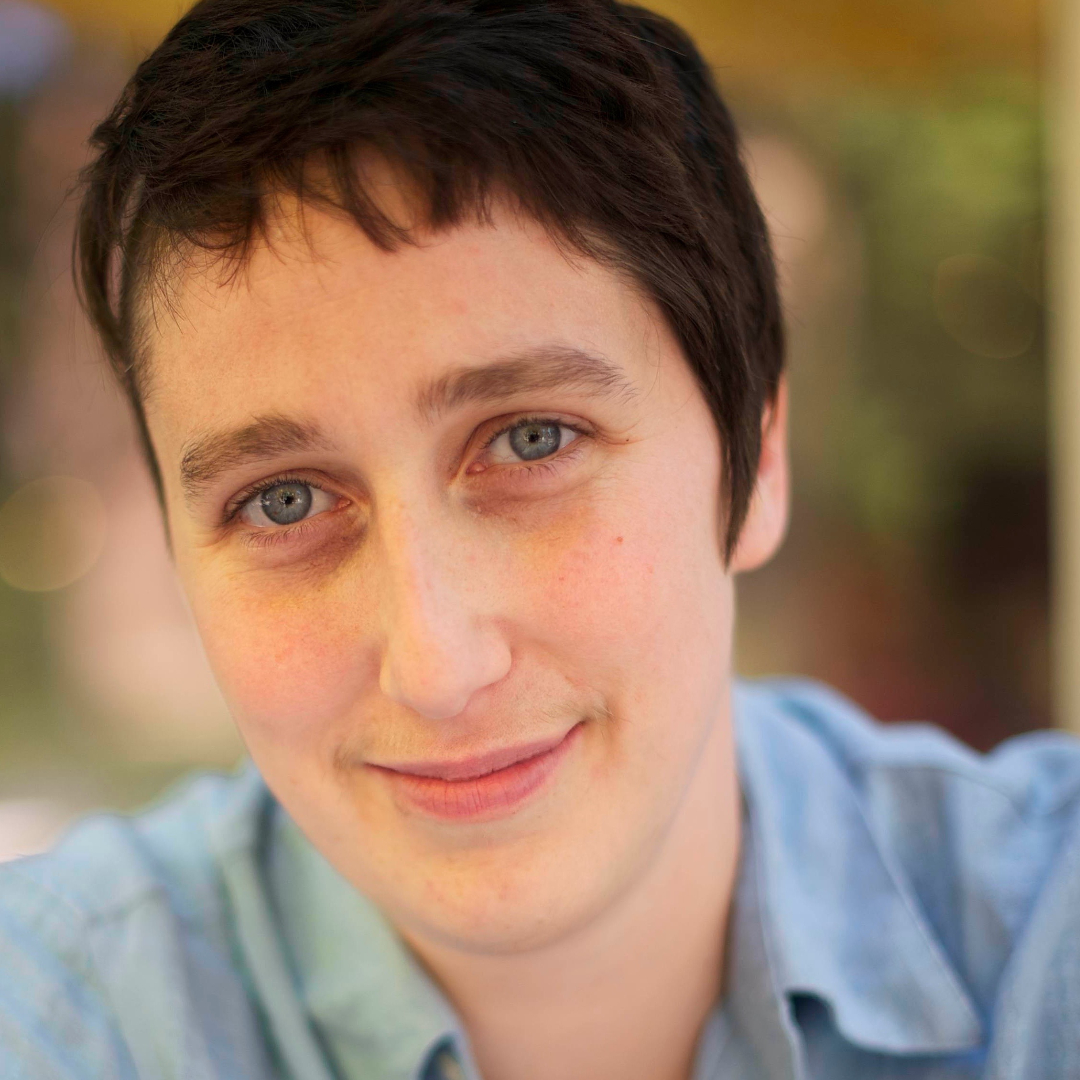 caucasian person with short brown hair wearing a  blue shirt smiles into camera