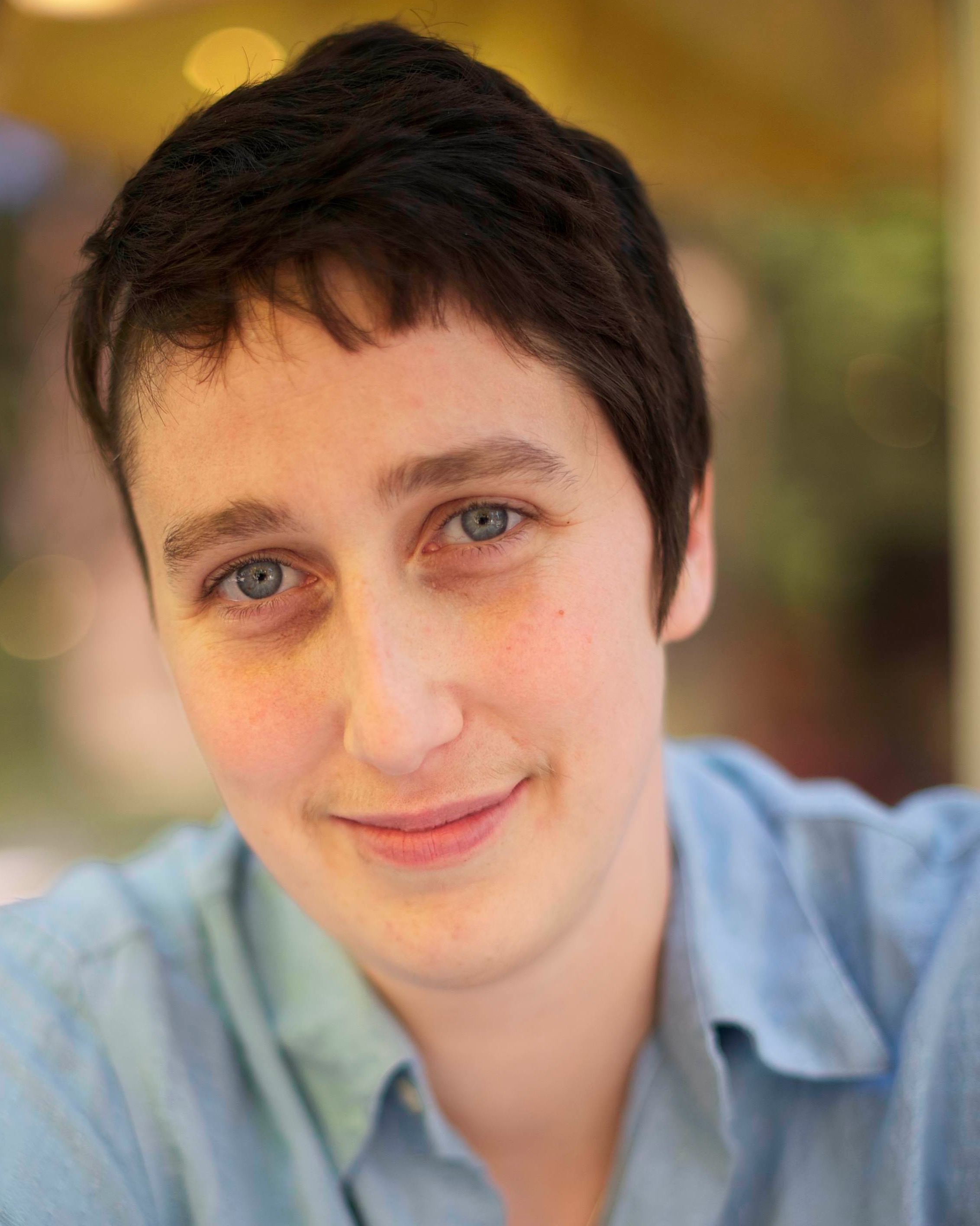 caucasian person with short brown hair wearing a  blue shirt smiles into camera