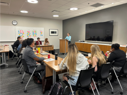 A classroom shot shows a speaker at a podium addressing students