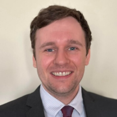 A headshot of Andrew Sawyers shows his smiling into the camera against a light background, wearing a suit and tie