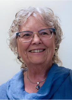 A woman with glasses and short grey hair smiling in a brightly lit room.