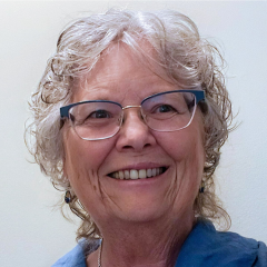 A woman with glasses and short grey hair smiling in a brightly lit room.