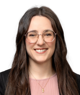 Portrait of a smiling individual with long hair, wearing round glasses and a pink top.