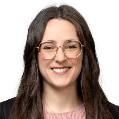 Portrait of a smiling individual with long hair, wearing round glasses and a pink top.