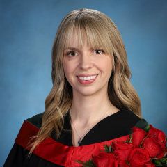 Taylor Tallent smiles at the camera against a blue backdrop, wearing a black graduation robe and holding a bouquet of red roses