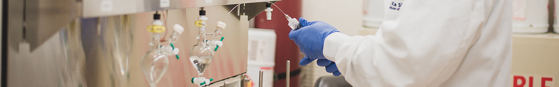 A technician is squeezing liquid from a large syringe into test tubes connected to lab equipment