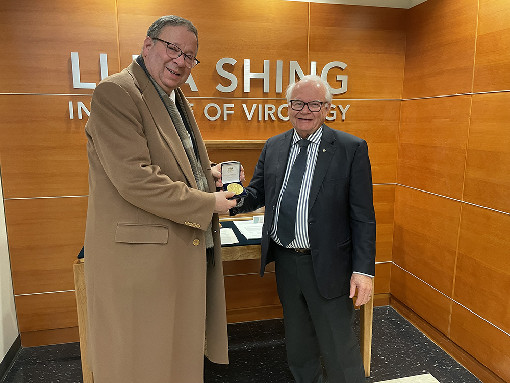 David Cohen poses with Dr. Lorne Tyrrell while holding the Nobel Prize medal in his hands