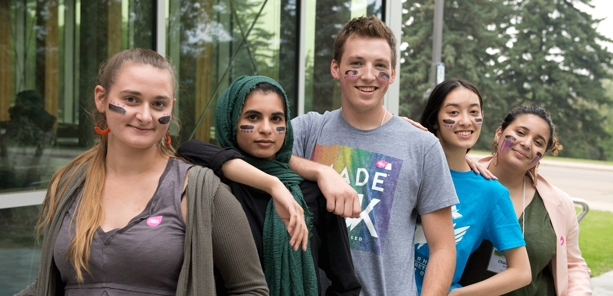 five students pose together with matching facepaint outside of peter lougheed hall