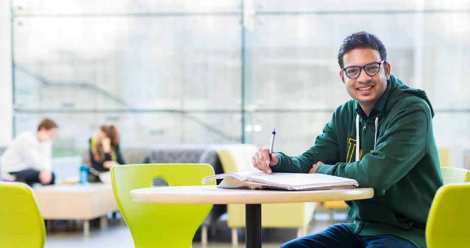 A person sitting in front of a computer, writing in a notebook