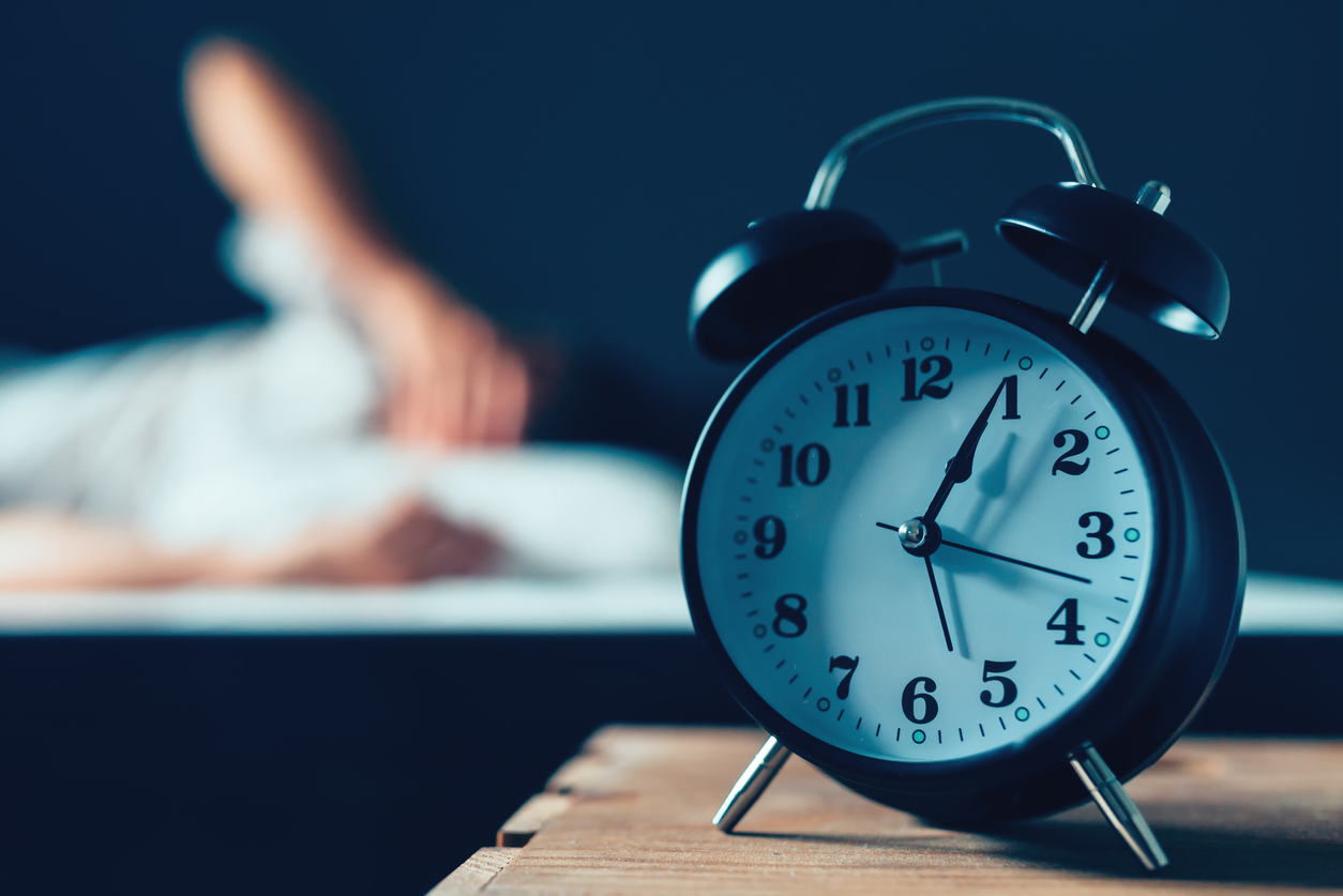 Clock on a nightstand as a person struggles to sleep