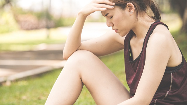 Young woman sitting on ground with hand on head